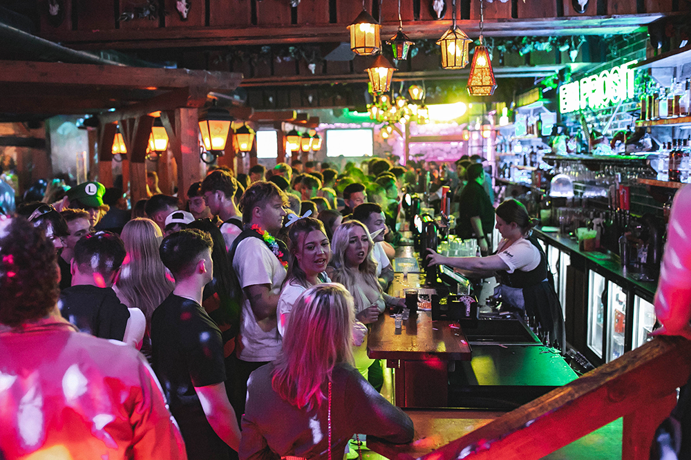 Crowd shot of people at the bar. Wooden booths can be seen to the right with glowing lanterns above.